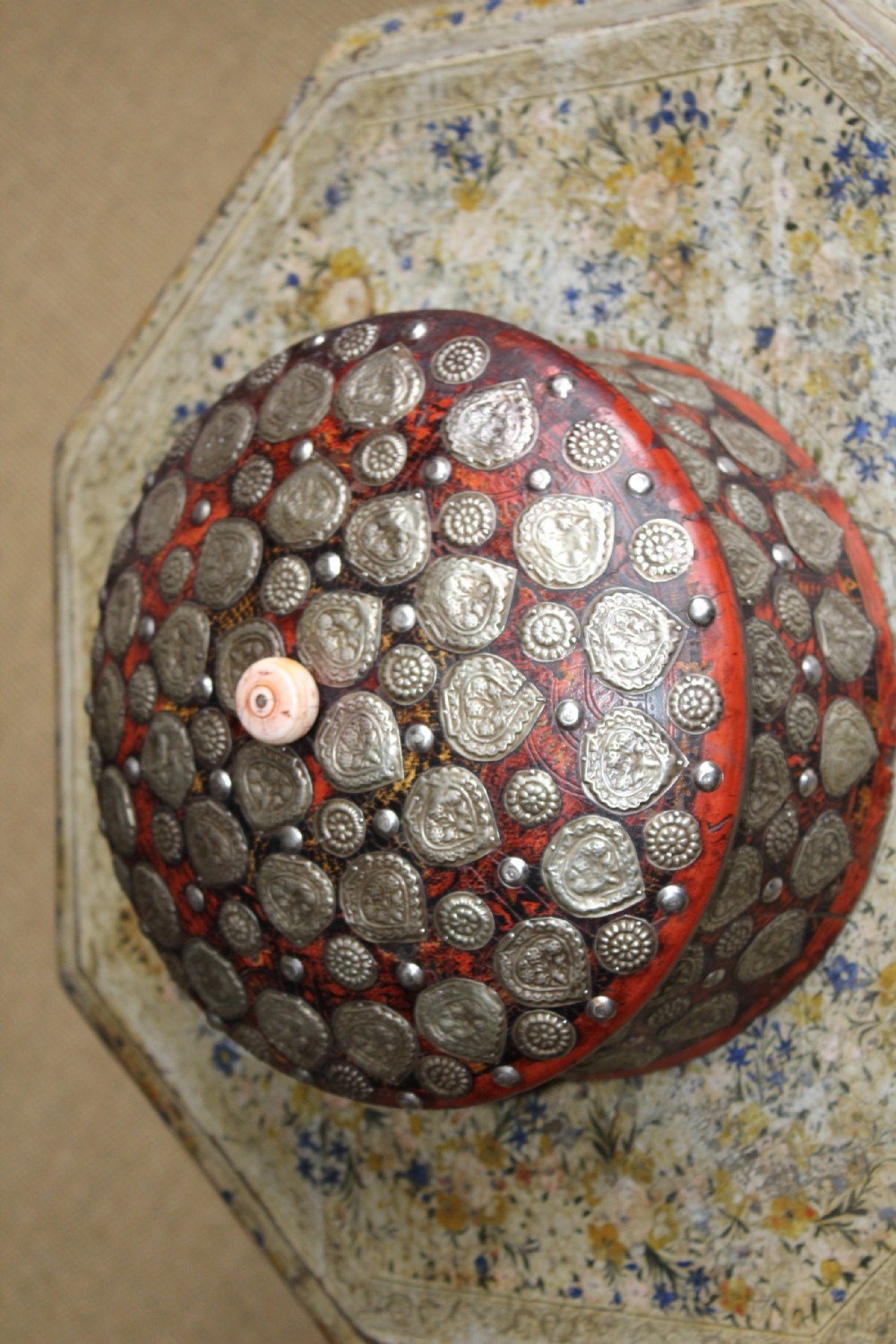 A circular red lacquered Kashmiri turban box with a domed lid, adorned with embossed silver-coloured metal mounts and a central turned knob. View V