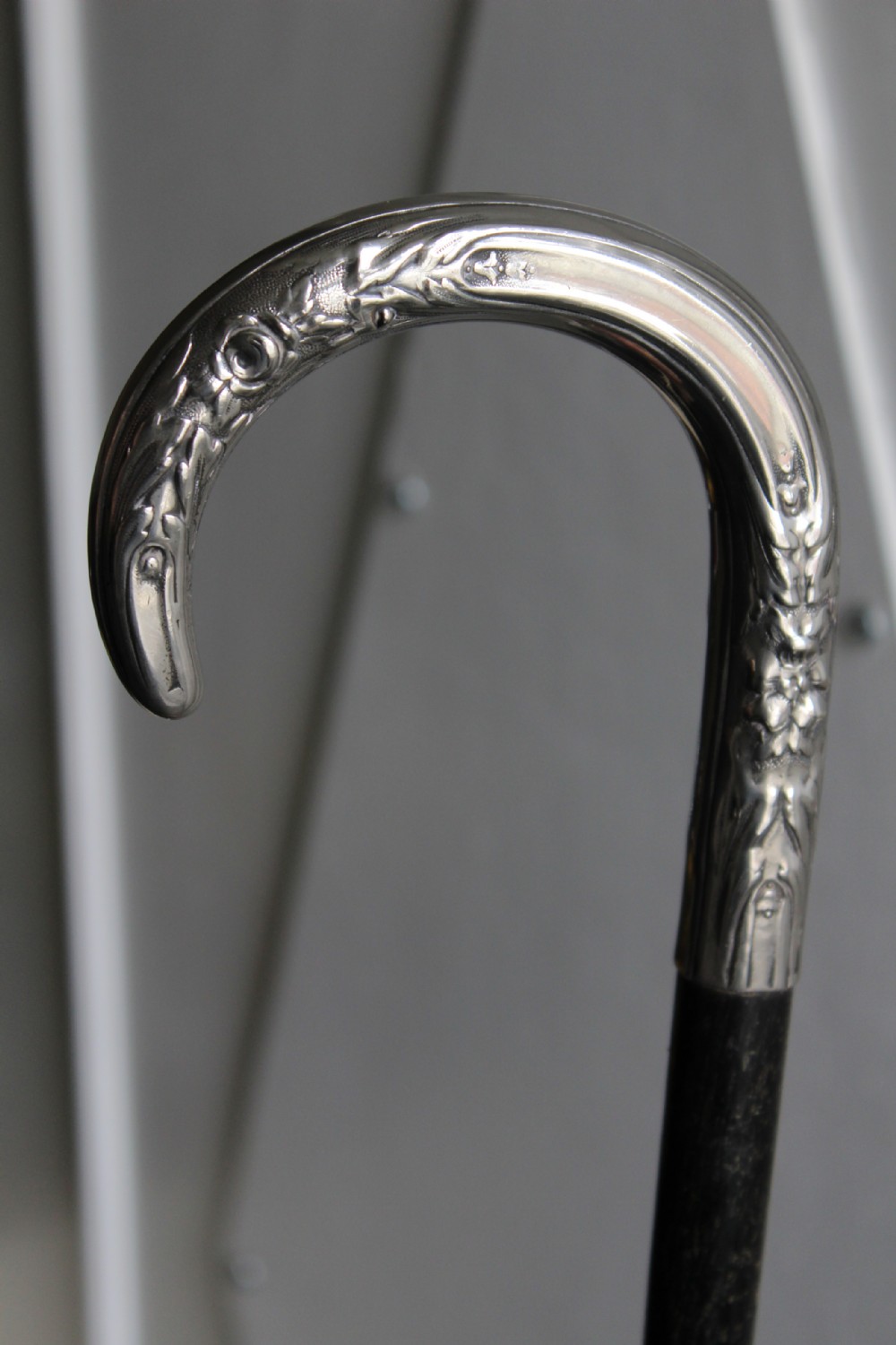 An ebonised oak walking stick featuring a silver-coloured crook handle embossed with floral and scroll patterns.