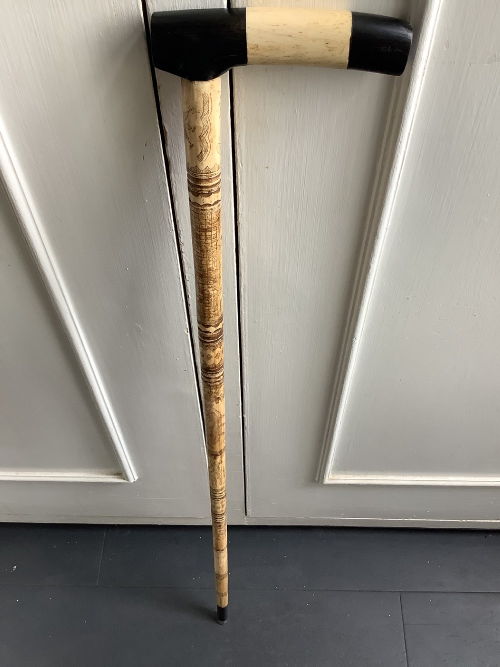 A maritime walking stick featuring a carved scrimshaw shaft with geometric patterns and a T-bar handle made of cream bone and black end caps. View II