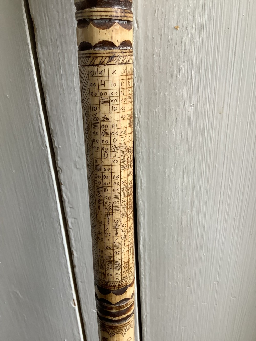 A maritime walking stick featuring a carved scrimshaw shaft with geometric patterns and a T-bar handle made of cream bone and black end caps. View III