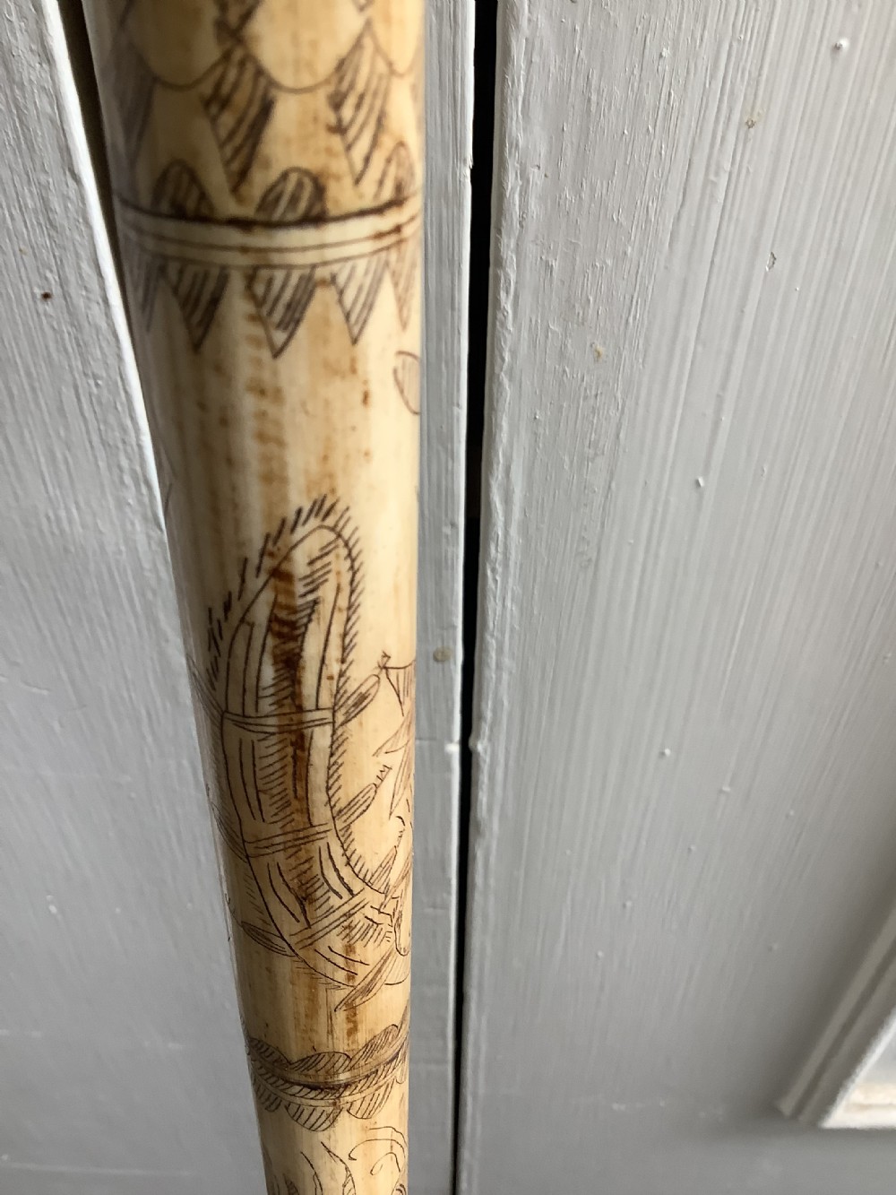 A maritime walking stick featuring a carved scrimshaw shaft with geometric patterns and a T-bar handle made of cream bone and black end caps. View IV