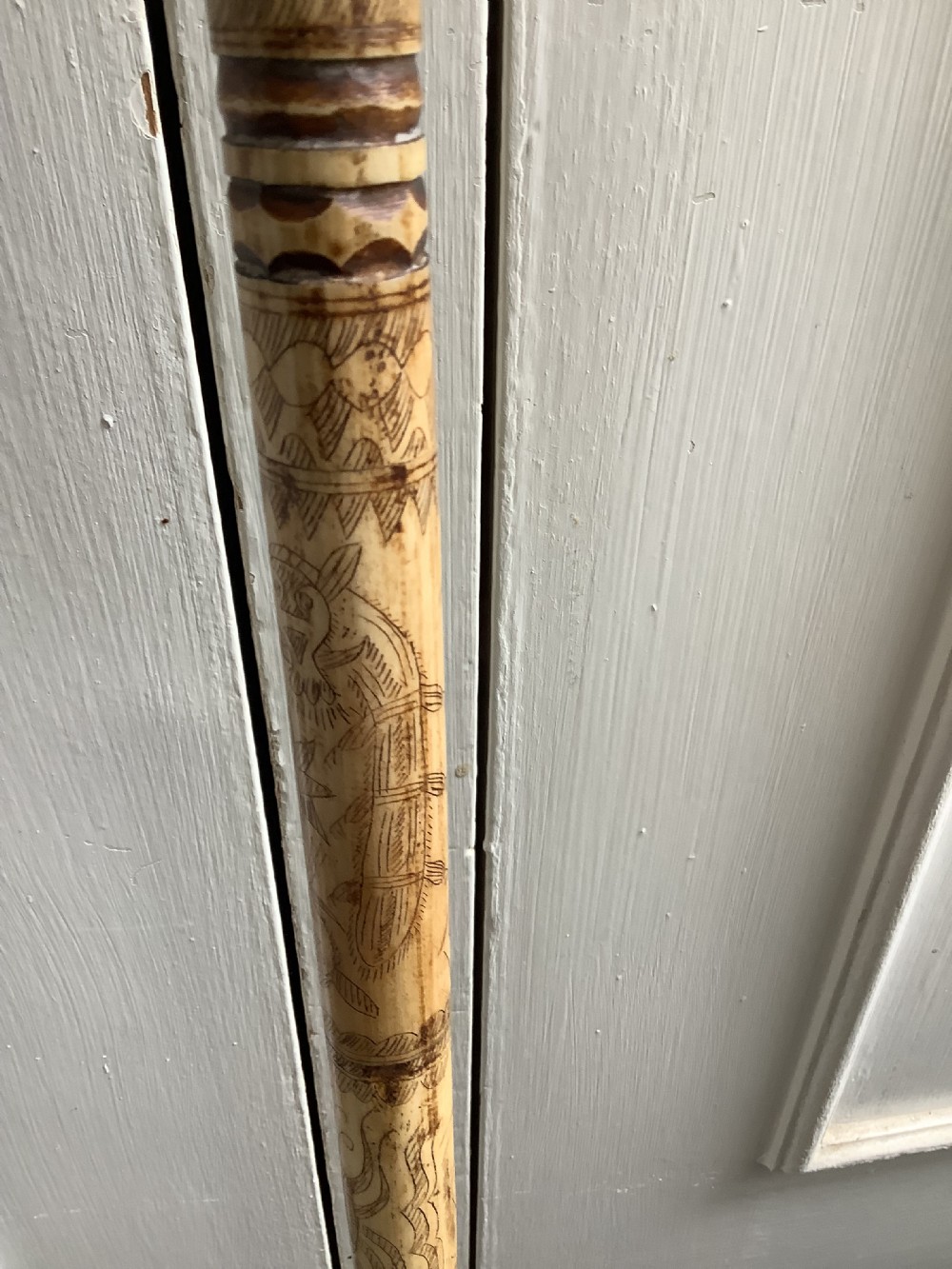 A maritime walking stick featuring a carved scrimshaw shaft with geometric patterns and a T-bar handle made of cream bone and black end caps. View V
