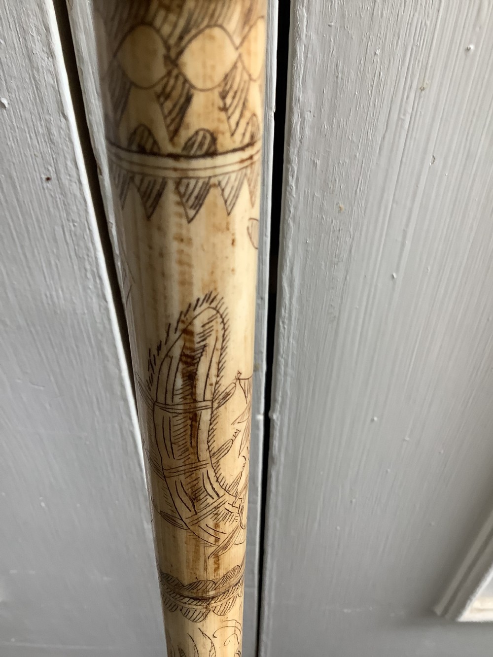A maritime walking stick featuring a carved scrimshaw shaft with geometric patterns and a T-bar handle made of cream bone and black end caps. View VII
