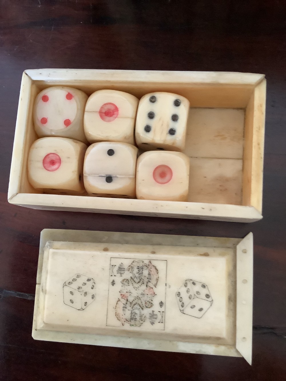 A small rectangular carved bone box containing six hand-carved bone dice with a sliding lid decorated with an etched playing card image.