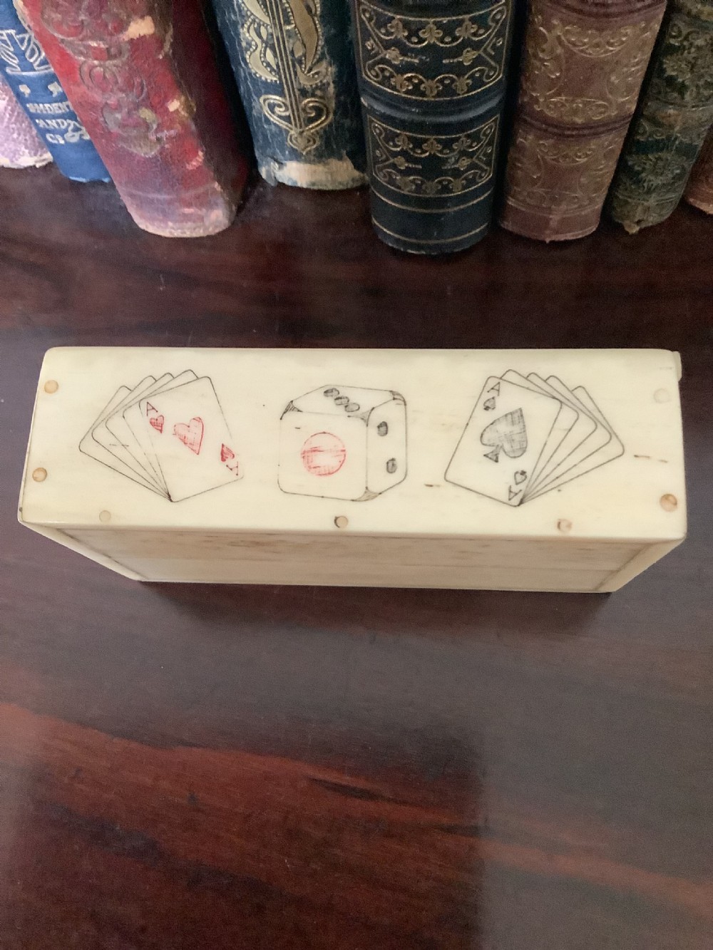 A small rectangular carved bone box containing six hand-carved bone dice with a sliding lid decorated with an etched playing card image. View IV