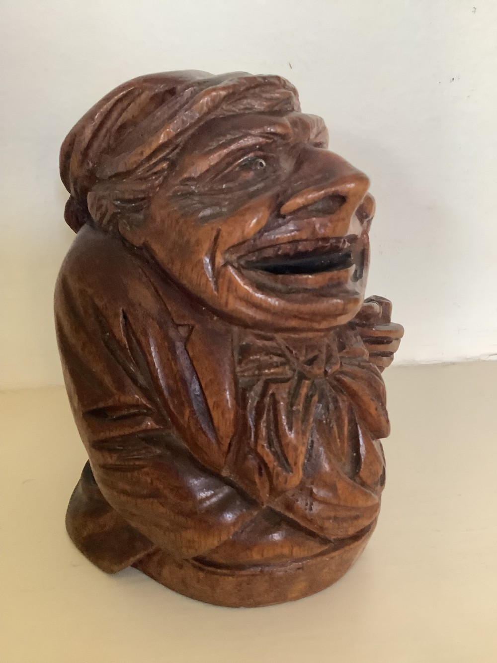 A hand-carved dark hardwood money box sculpted in the shape of a smiling miser figure with a coin slot in its mouth.