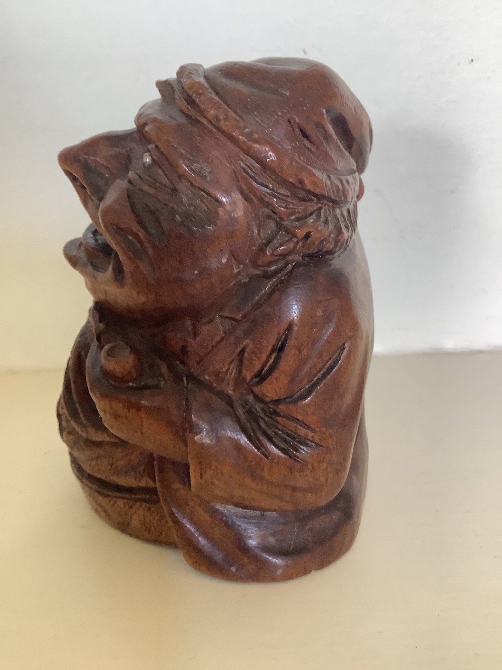 A hand-carved dark hardwood money box sculpted in the shape of a smiling miser figure with a coin slot in its mouth. View II