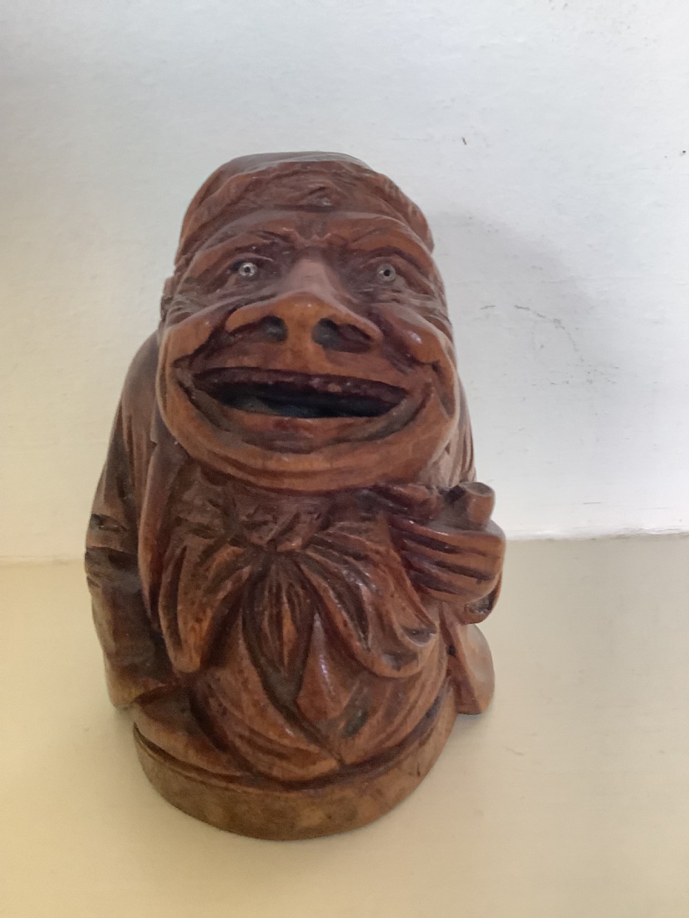 A hand-carved dark hardwood money box sculpted in the shape of a smiling miser figure with a coin slot in its mouth. View III