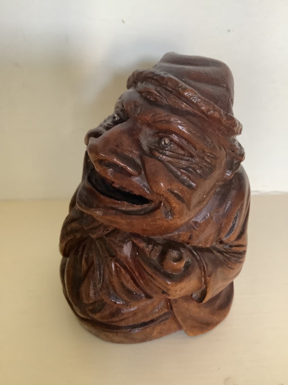A hand-carved dark hardwood money box sculpted in the shape of a smiling miser figure with a coin slot in its mouth. View IV