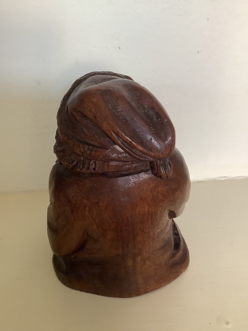 A hand-carved dark hardwood money box sculpted in the shape of a smiling miser figure with a coin slot in its mouth. View V