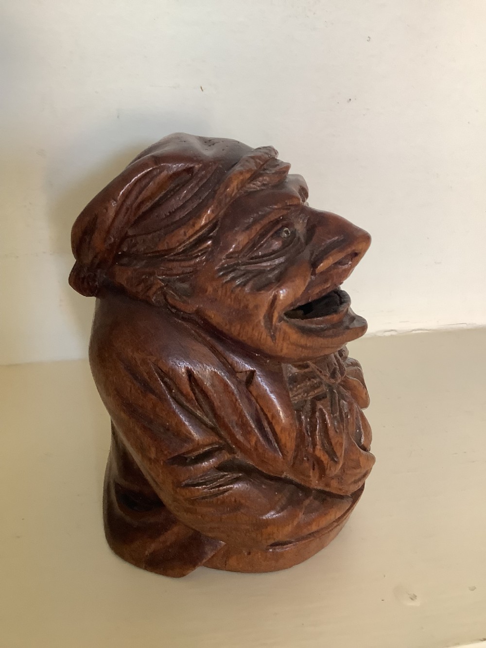 A hand-carved dark hardwood money box sculpted in the shape of a smiling miser figure with a coin slot in its mouth. View VI