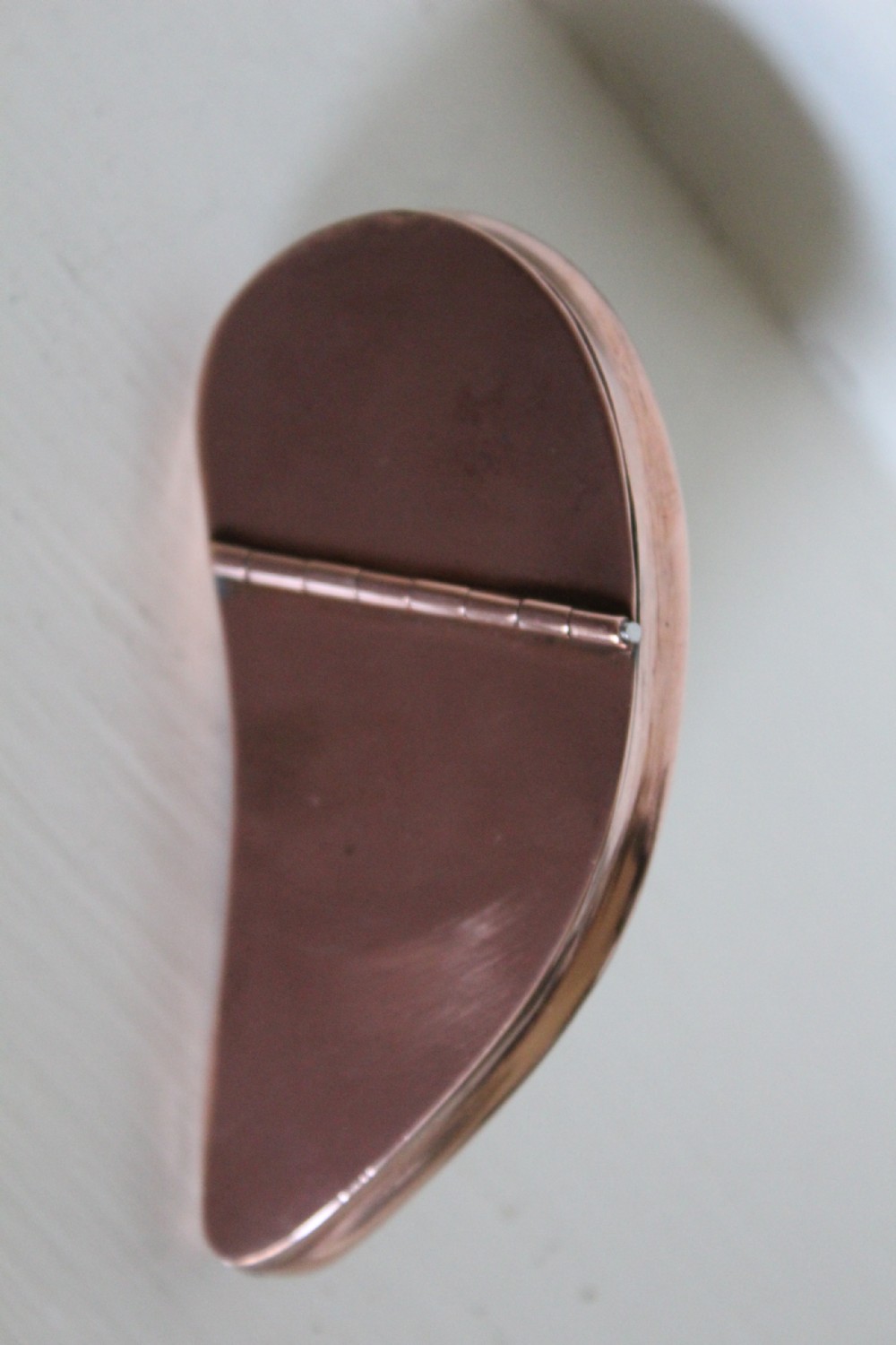 An antique mussel shell pocket snuff box with polished dark purple and brown concentric growth lines framed by a copper metal rim. View VI