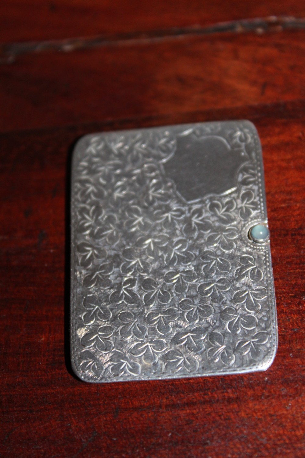 A small rectangular sterling silver stamp case featuring an engraved clover motif and a cabochon push clasp.