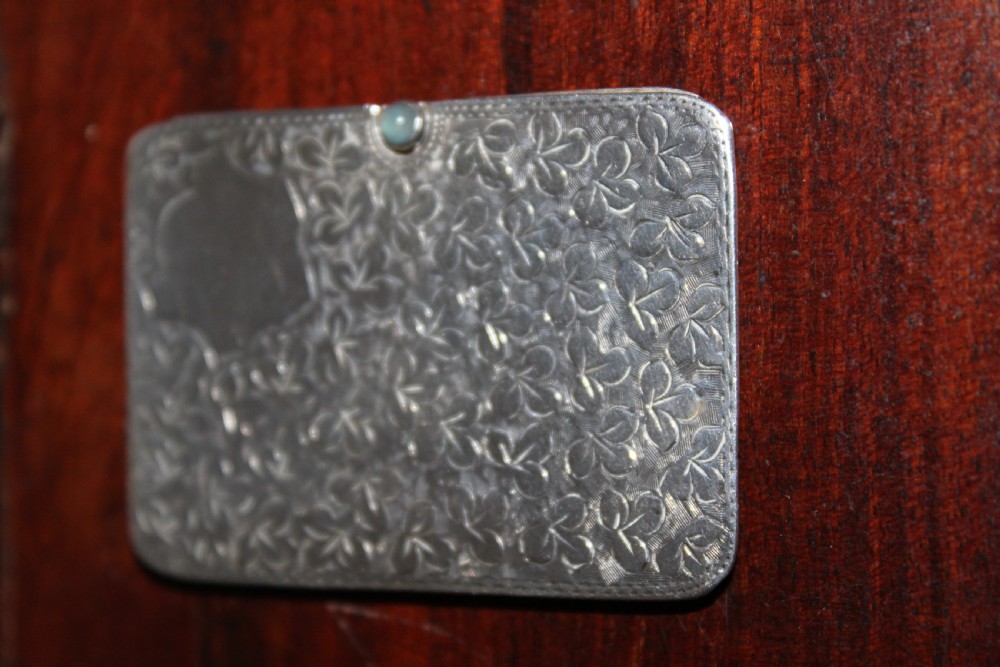 A small rectangular sterling silver stamp case featuring an engraved clover motif and a cabochon push clasp. View V