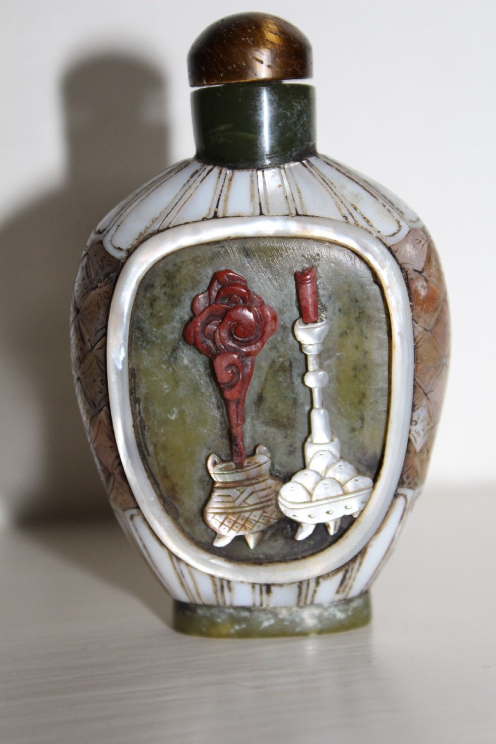 A 19th-century Chinese snuff bottle featuring a carved stone figure inset within a mother-of-pearl frame on a green jade body. View II