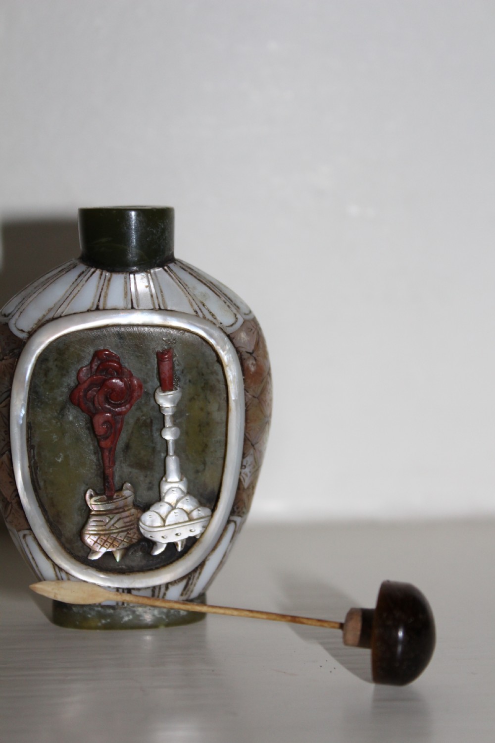 A 19th-century Chinese snuff bottle featuring a carved stone figure inset within a mother-of-pearl frame on a green jade body. View III