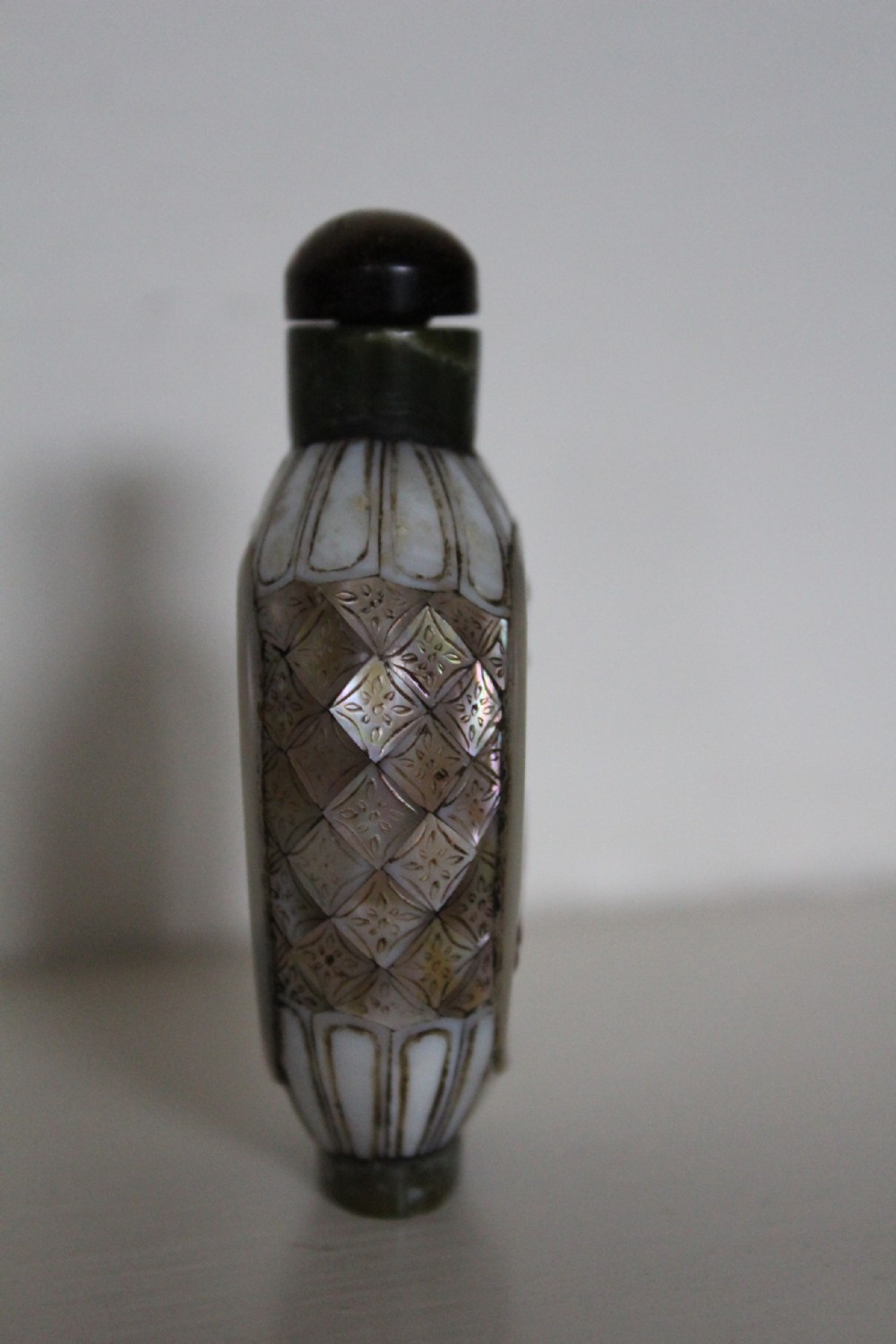 A 19th-century Chinese snuff bottle featuring a carved stone figure inset within a mother-of-pearl frame on a green jade body. View IV