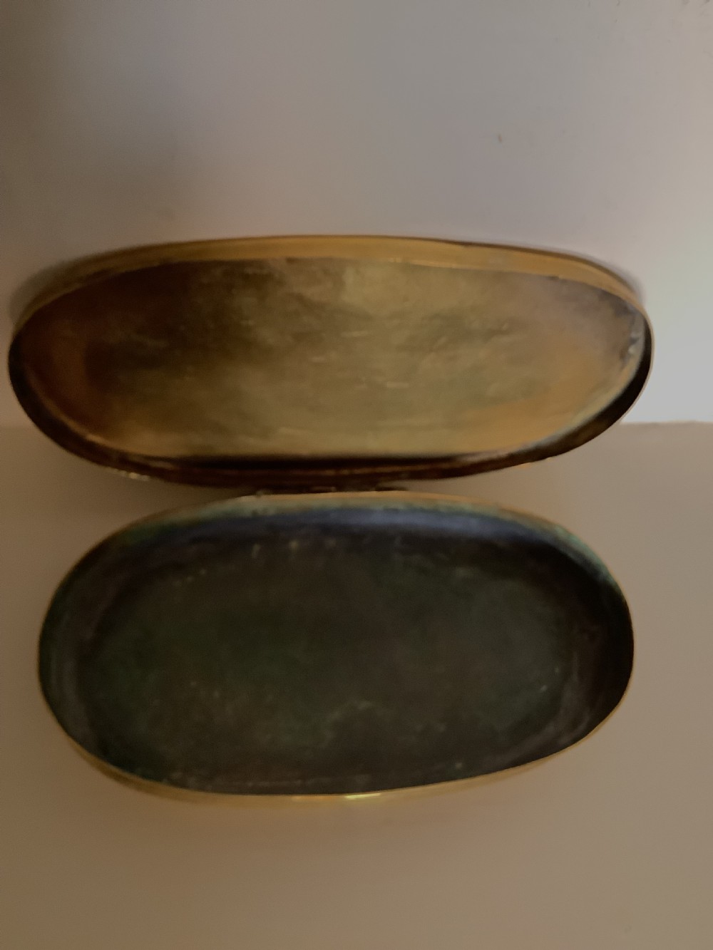 An oval heavy-gauge brass tobacco box lid featuring relief-engraved panels with cherub figures and scrollwork. View VII