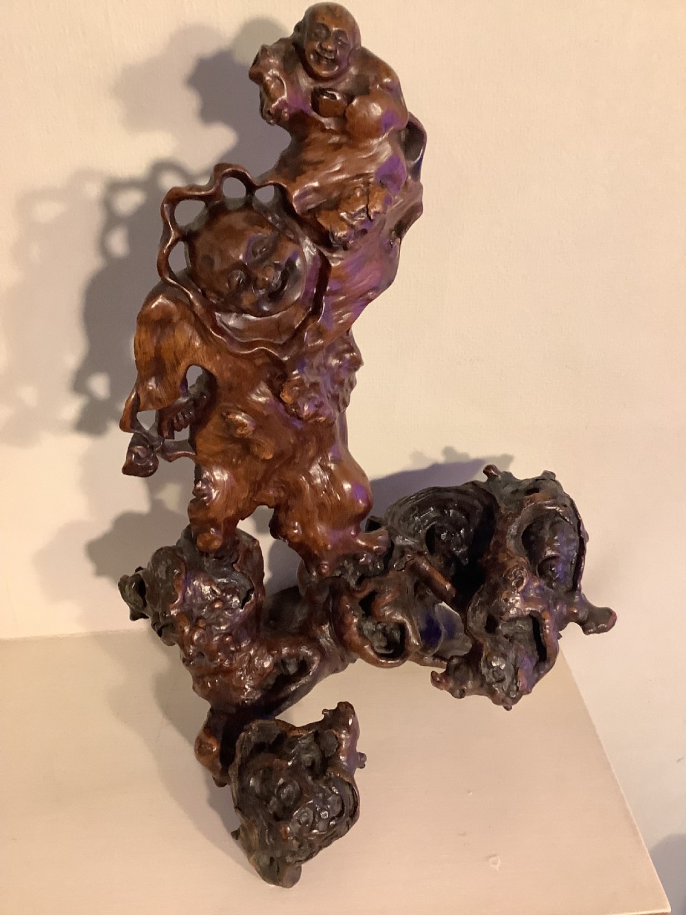 A carved dark brown rootwood sculpture depicting a smiling man carrying a child on his shoulders, integrated into the natural gnarled shape of the wood root.