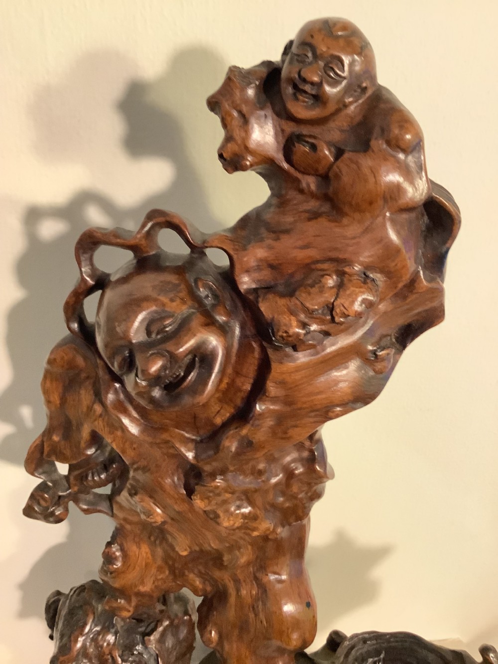 A carved dark brown rootwood sculpture depicting a smiling man carrying a child on his shoulders, integrated into the natural gnarled shape of the wood root. View II