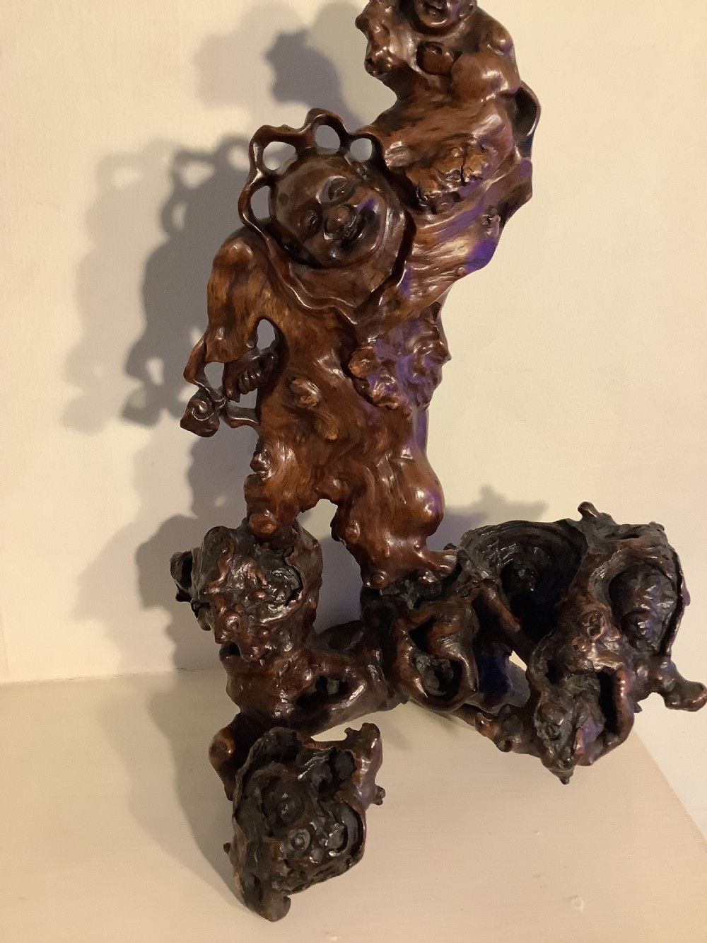 A carved dark brown rootwood sculpture depicting a smiling man carrying a child on his shoulders, integrated into the natural gnarled shape of the wood root. View III