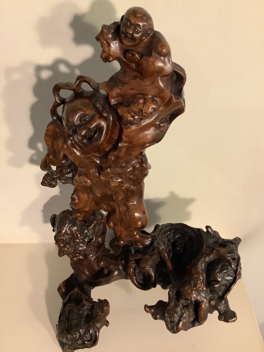 A carved dark brown rootwood sculpture depicting a smiling man carrying a child on his shoulders, integrated into the natural gnarled shape of the wood root. View IX