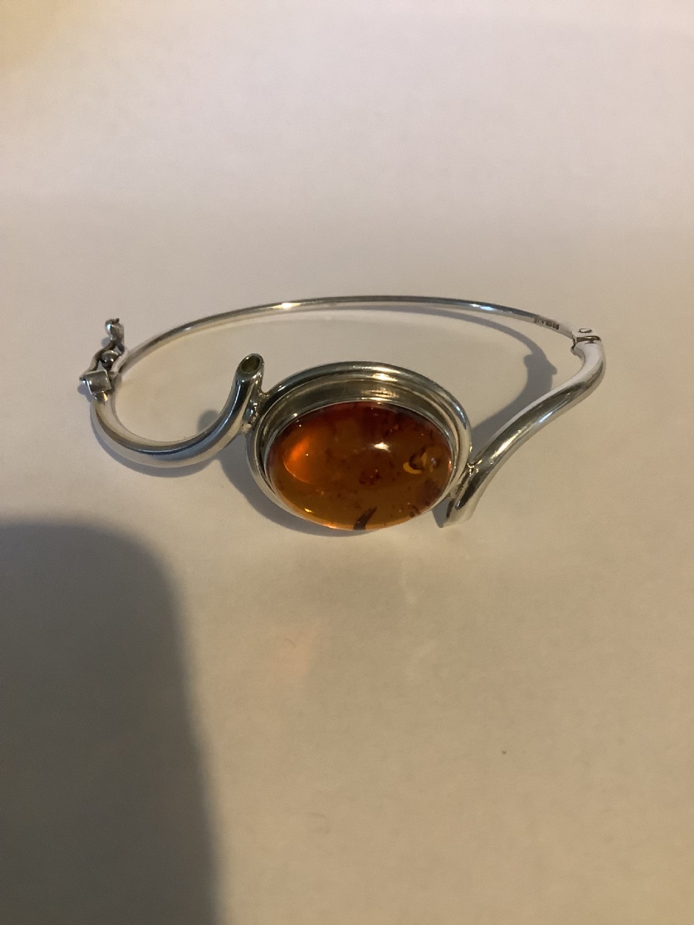 A sterling silver bracelet featuring a central oval bezel-set amber cabochon framed by contoured silver wire loops. View II