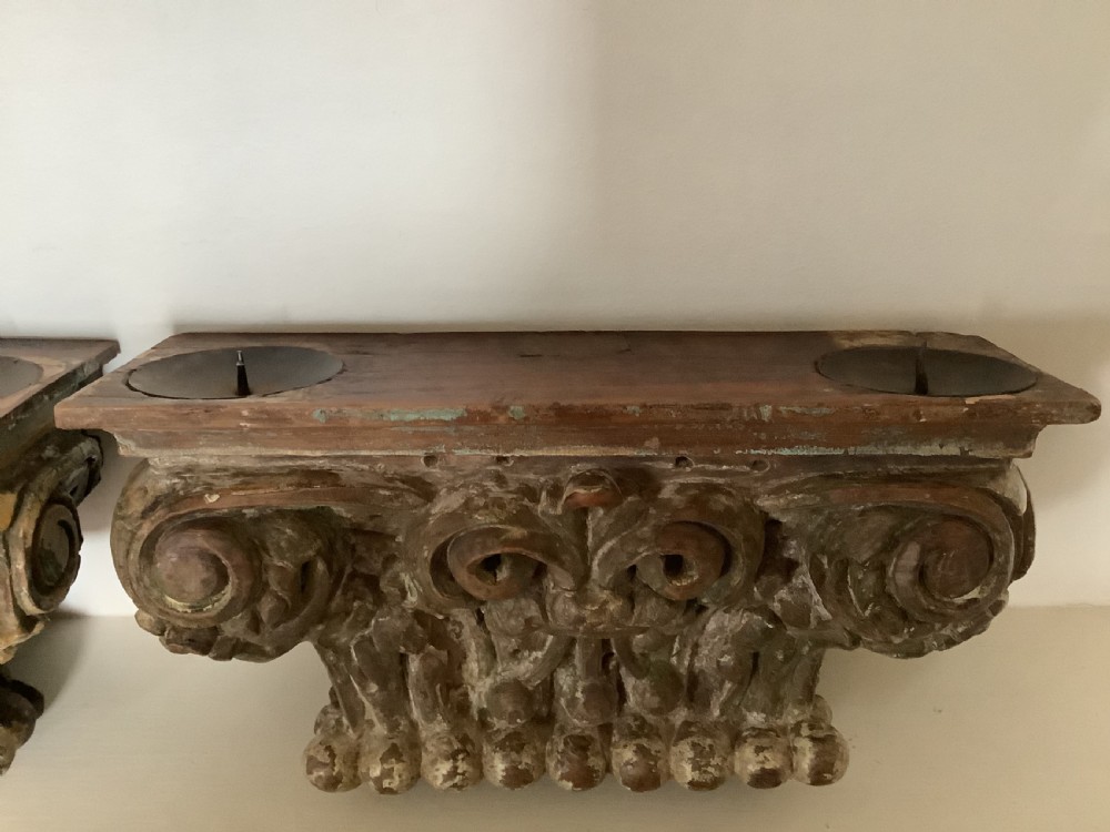 A pair of carved wooden Corinthian architectural capitals featuring acanthus leaf motifs and distressed painted finishes with metal candle inserts on top. View VIII
