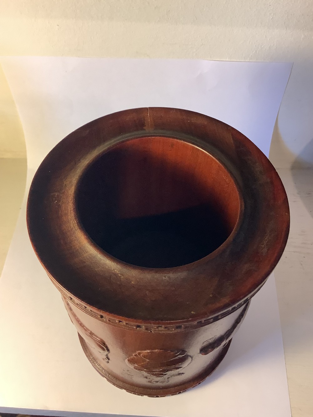 A cylindrical carved reddish brown hardwood Chinese brush pot decorated with high relief figures and an ox, bordered by geometric key fret patterns at the top and bottom edges. View VI
