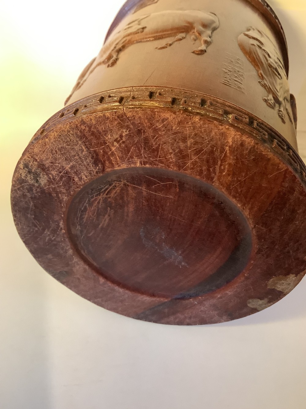 A cylindrical carved reddish brown hardwood Chinese brush pot decorated with high relief figures and an ox, bordered by geometric key fret patterns at the top and bottom edges. View VII