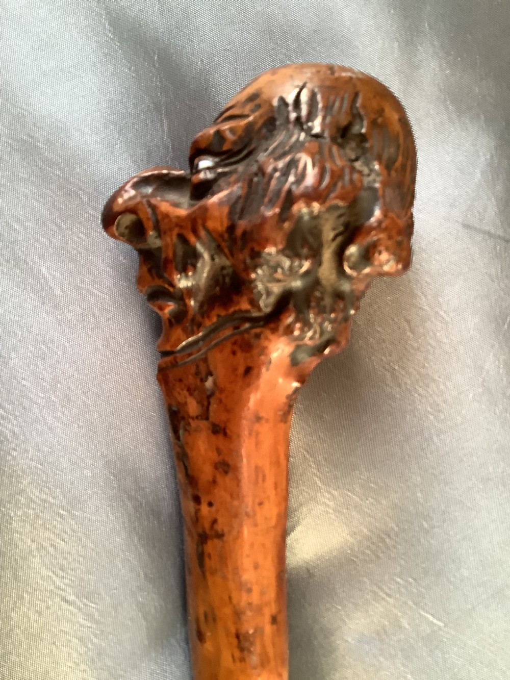 A close-up view of a warm brown hand-carved wooden stick top depicting a detailed caricature face with prominent facial features.