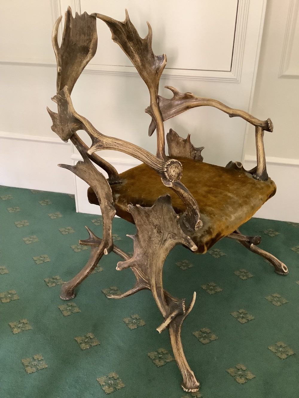 An antique Black Forest armchair constructed with interlocking natural deer antlers and a warm brown velvet upholstered seat.