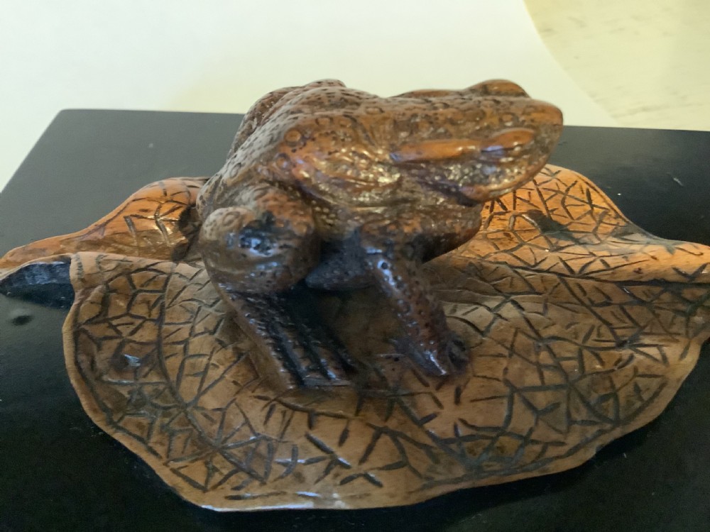 A carved brown boxwood toad sitting on an etched leaf surface mounted on a black lacquered rectangular base. View III