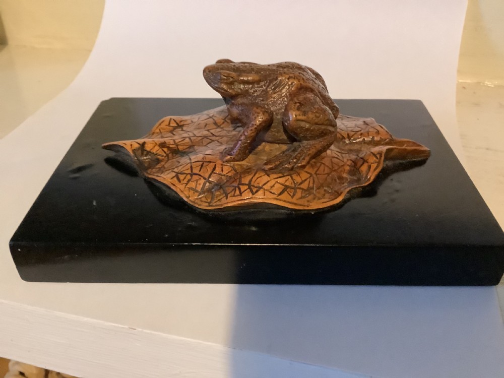 A carved brown boxwood toad sitting on an etched leaf surface mounted on a black lacquered rectangular base. View II