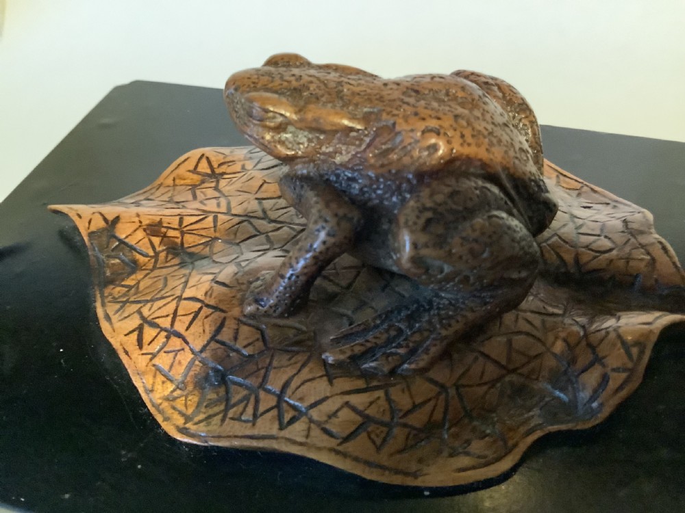 A carved brown boxwood toad sitting on an etched leaf surface mounted on a black lacquered rectangular base. View V