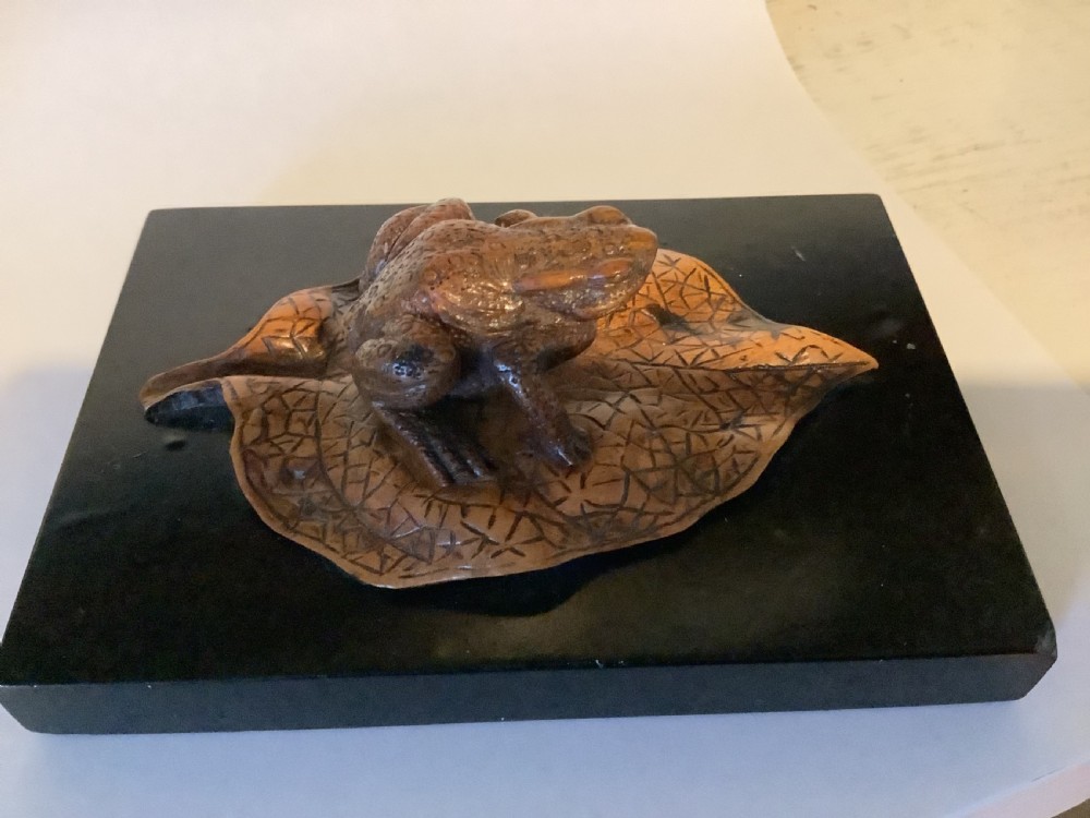 A carved brown boxwood toad sitting on an etched leaf surface mounted on a black lacquered rectangular base. View VI