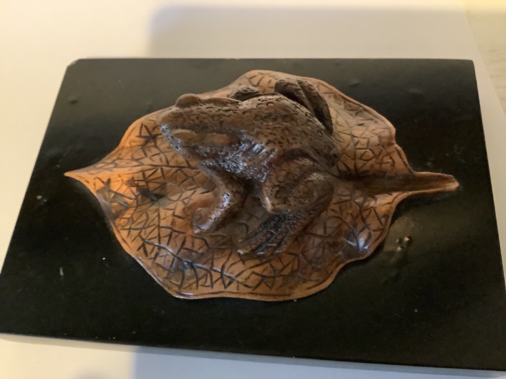 A carved brown boxwood toad sitting on an etched leaf surface mounted on a black lacquered rectangular base. View VIII