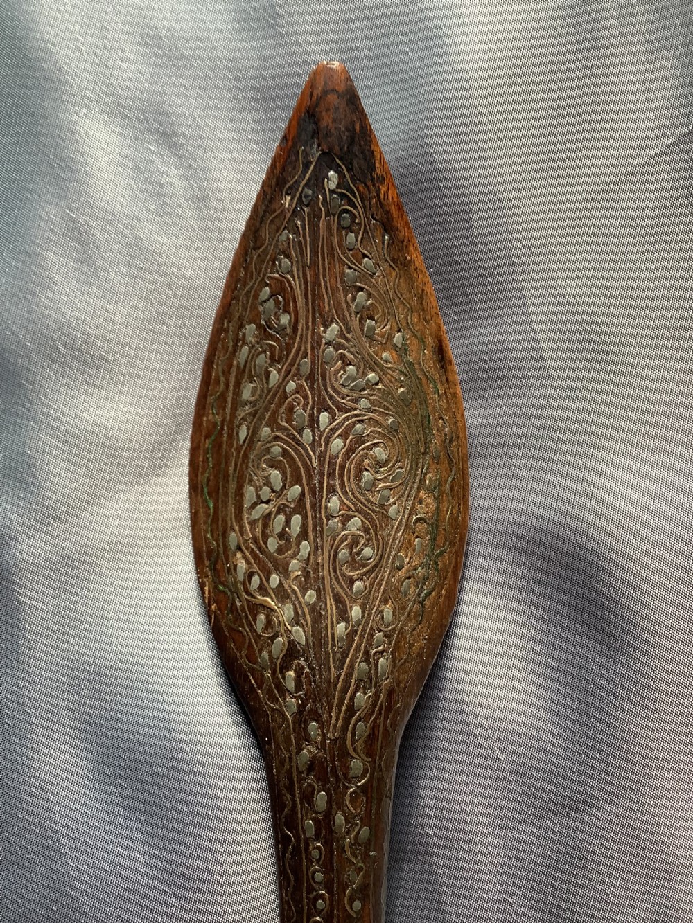 A carved dark wood back scratcher featuring a cross-hatched textured paddle head and delicate floral silver inlay along the slender handle. View V