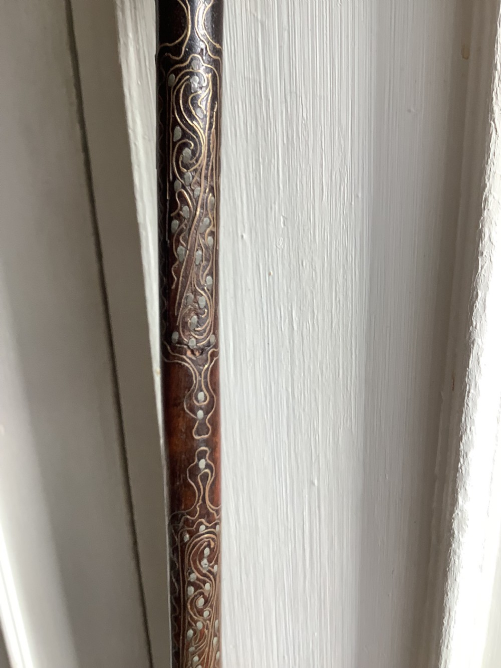 A carved dark wood back scratcher featuring a cross-hatched textured paddle head and delicate floral silver inlay along the slender handle. View X