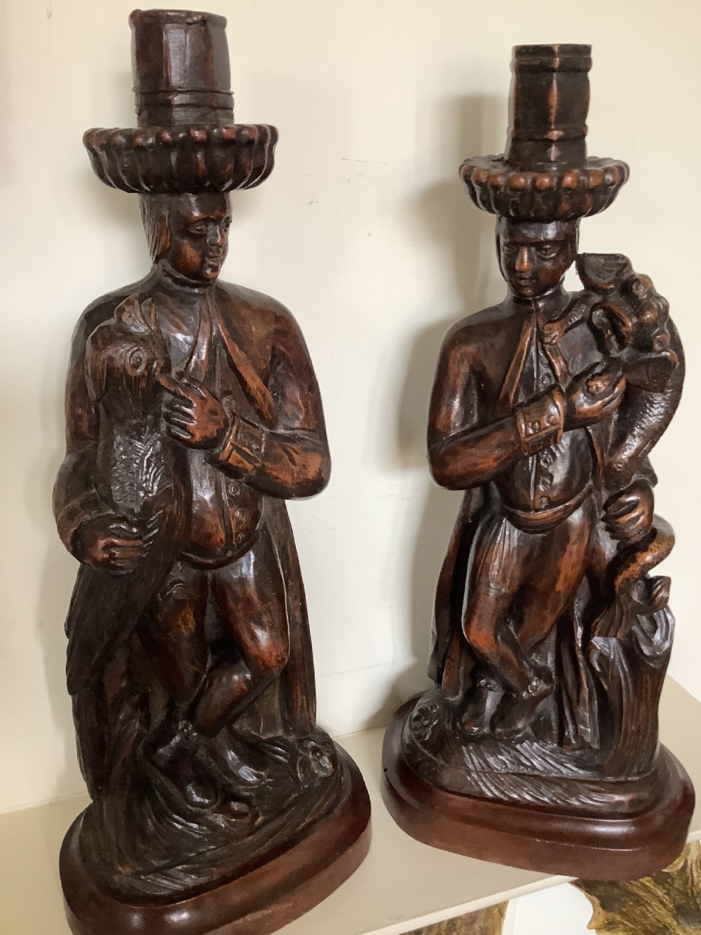 A pair of hand-carved dark wood candlesticks sculpted in the form of standing poachers holding game.