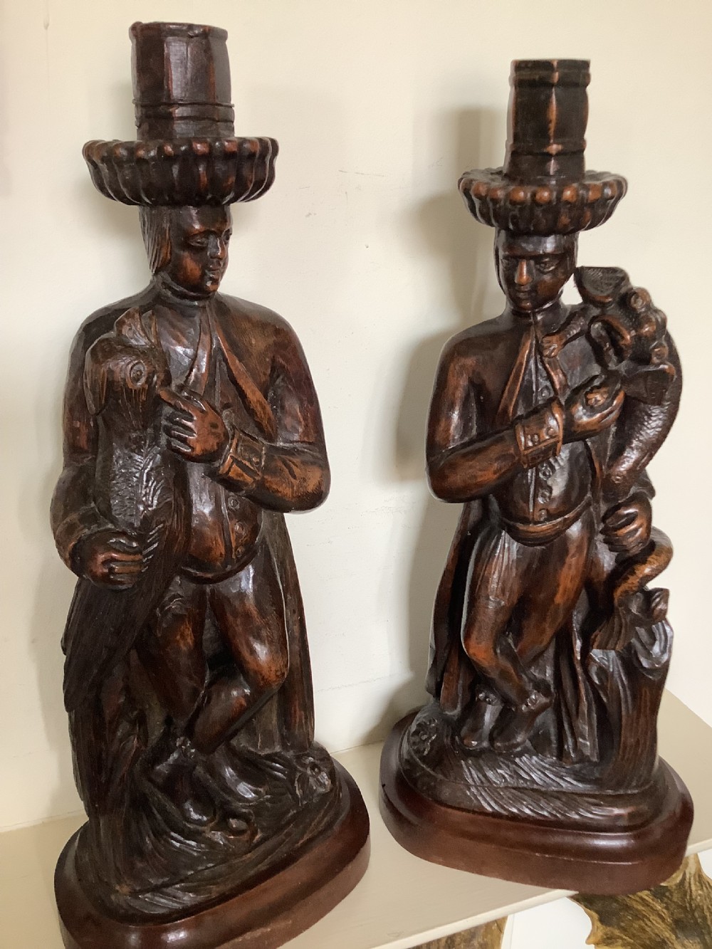 A pair of hand-carved dark wood candlesticks sculpted in the form of standing poachers holding game. View II