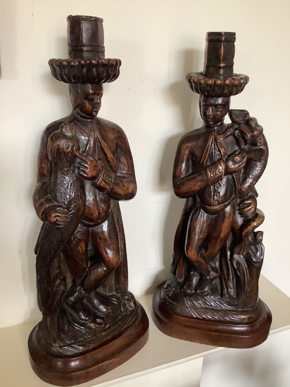 A pair of hand-carved dark wood candlesticks sculpted in the form of standing poachers holding game. View VI
