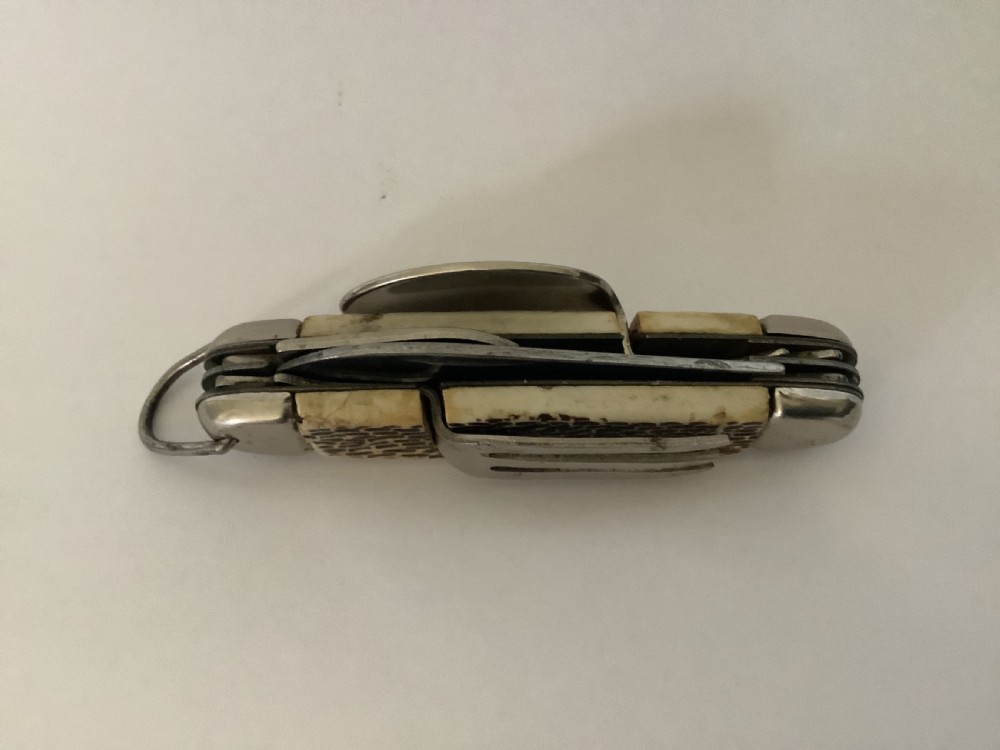 A vintage Jowika multi-blade camping pocket knife featuring an extended main blade, folded steel spoon, fork, bottle opener, and textured brown jigged bone handle scales. View V