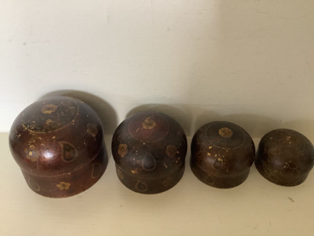 A set of four graduated round Kashmiri boxes painted in dark red and brown with gold floral and paisley motifs.