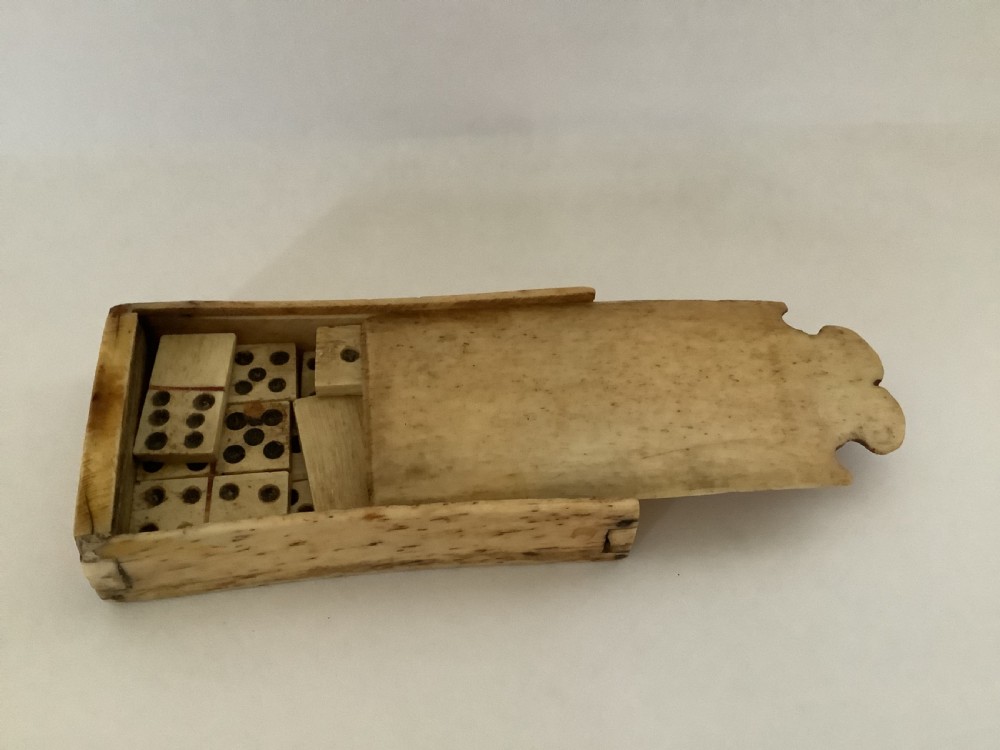 A hand-carved bone domino set featuring individual numbered tiles with incised dark pips next to a matching rectangular bone box with a sliding lid. View V