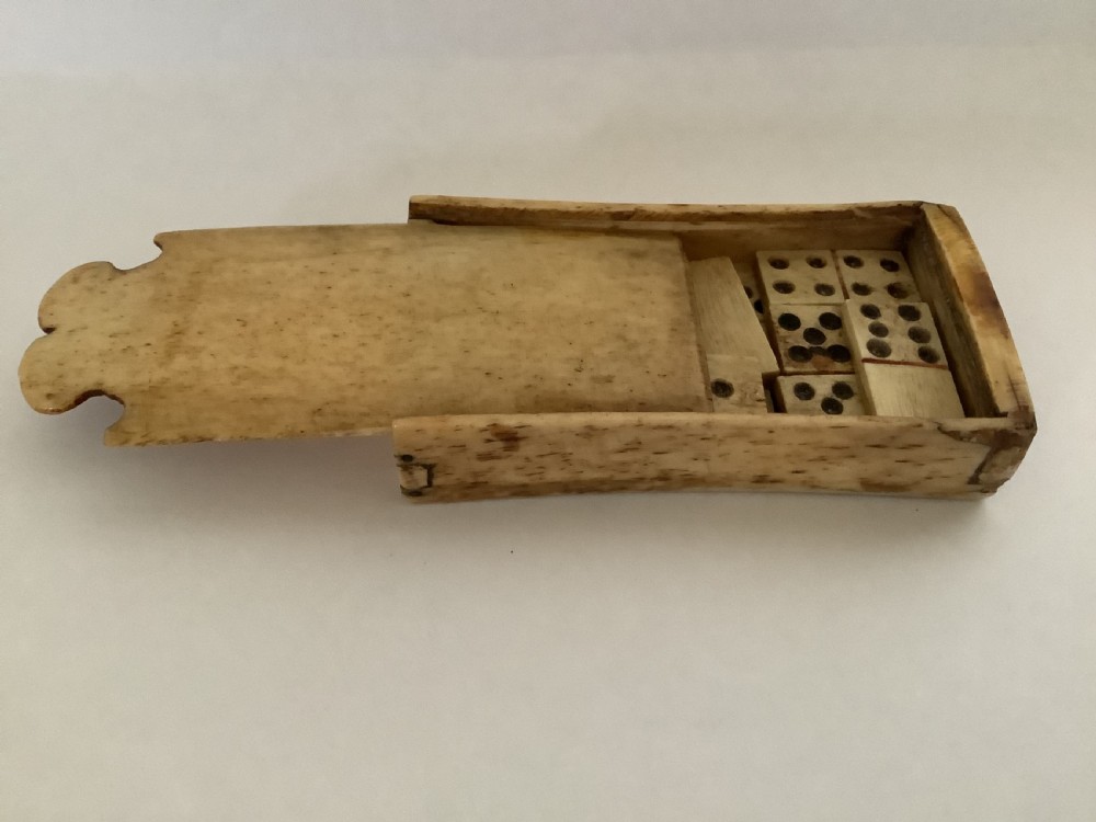A hand-carved bone domino set featuring individual numbered tiles with incised dark pips next to a matching rectangular bone box with a sliding lid. View II
