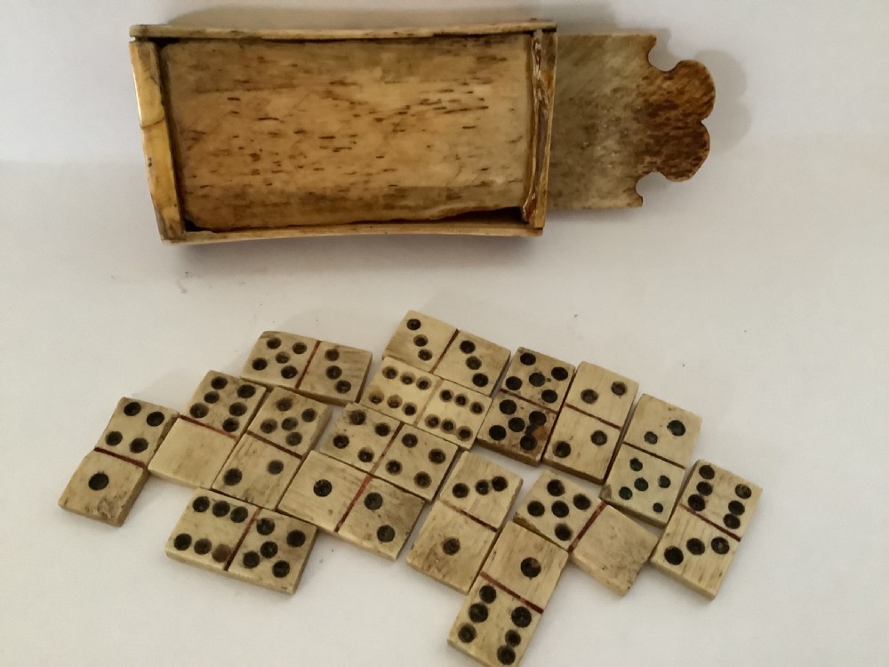 A hand-carved bone domino set featuring individual numbered tiles with incised dark pips next to a matching rectangular bone box with a sliding lid. View IV