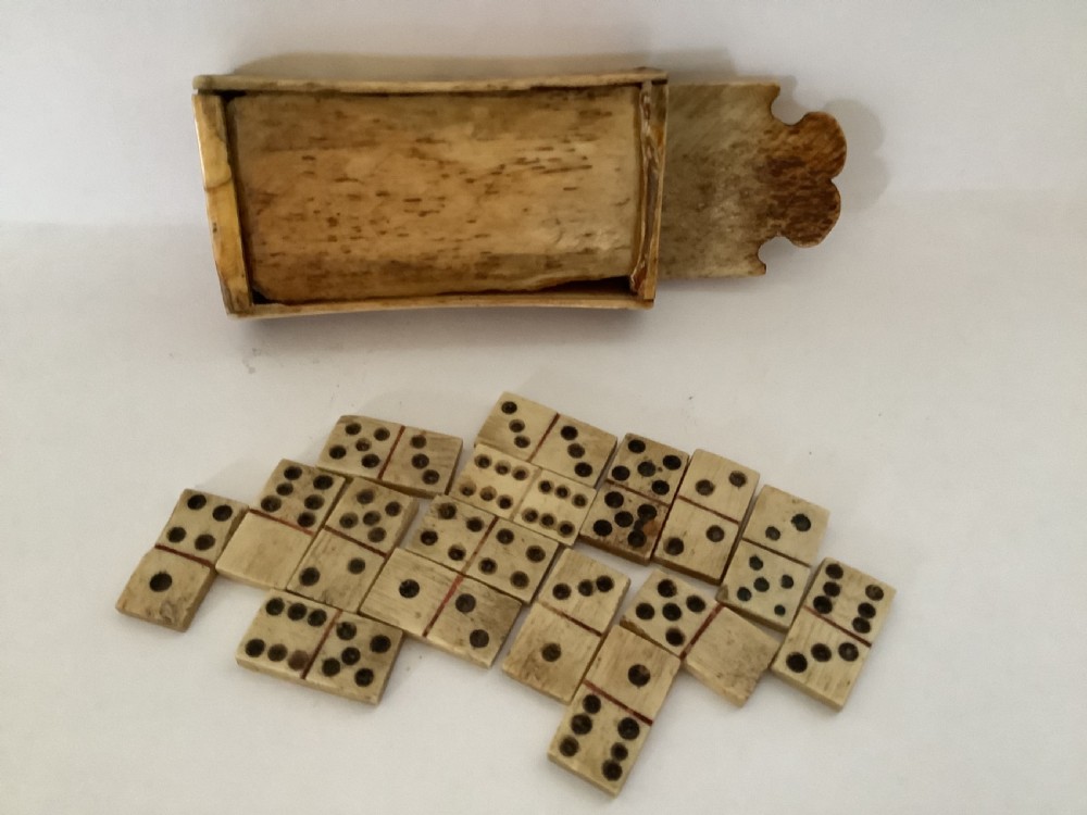 A hand-carved bone domino set featuring individual numbered tiles with incised dark pips next to a matching rectangular bone box with a sliding lid. View VI