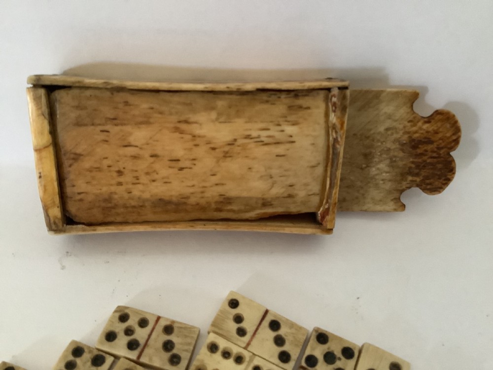 A hand-carved bone domino set featuring individual numbered tiles with incised dark pips next to a matching rectangular bone box with a sliding lid. View VII