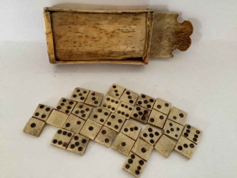 A hand-carved bone domino set featuring individual numbered tiles with incised dark pips next to a matching rectangular bone box with a sliding lid. View XI